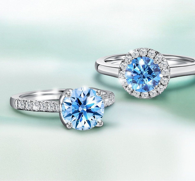 Two 1 carat diamond rings with round-cut blue gemstones, one in a diamond halo setting and the other with a diamond-paved band, set in white gold.