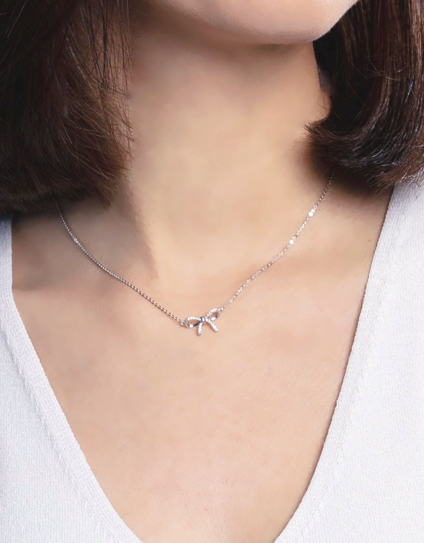 woman wearing LVC necklace designed with a bow encrusted with diamonds in white gold